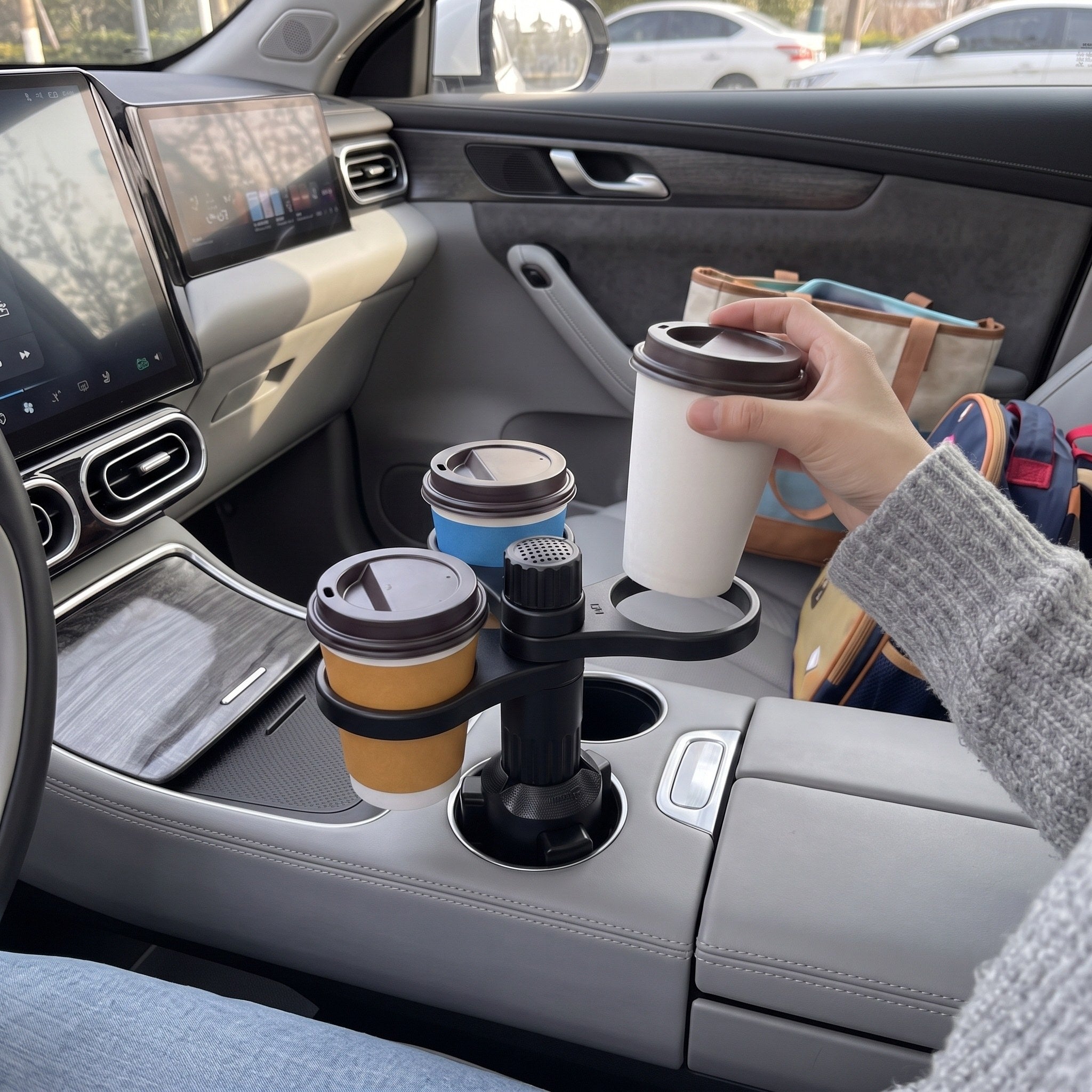 A hand lifts one takeaway cup from a ring in a parked grey SUV