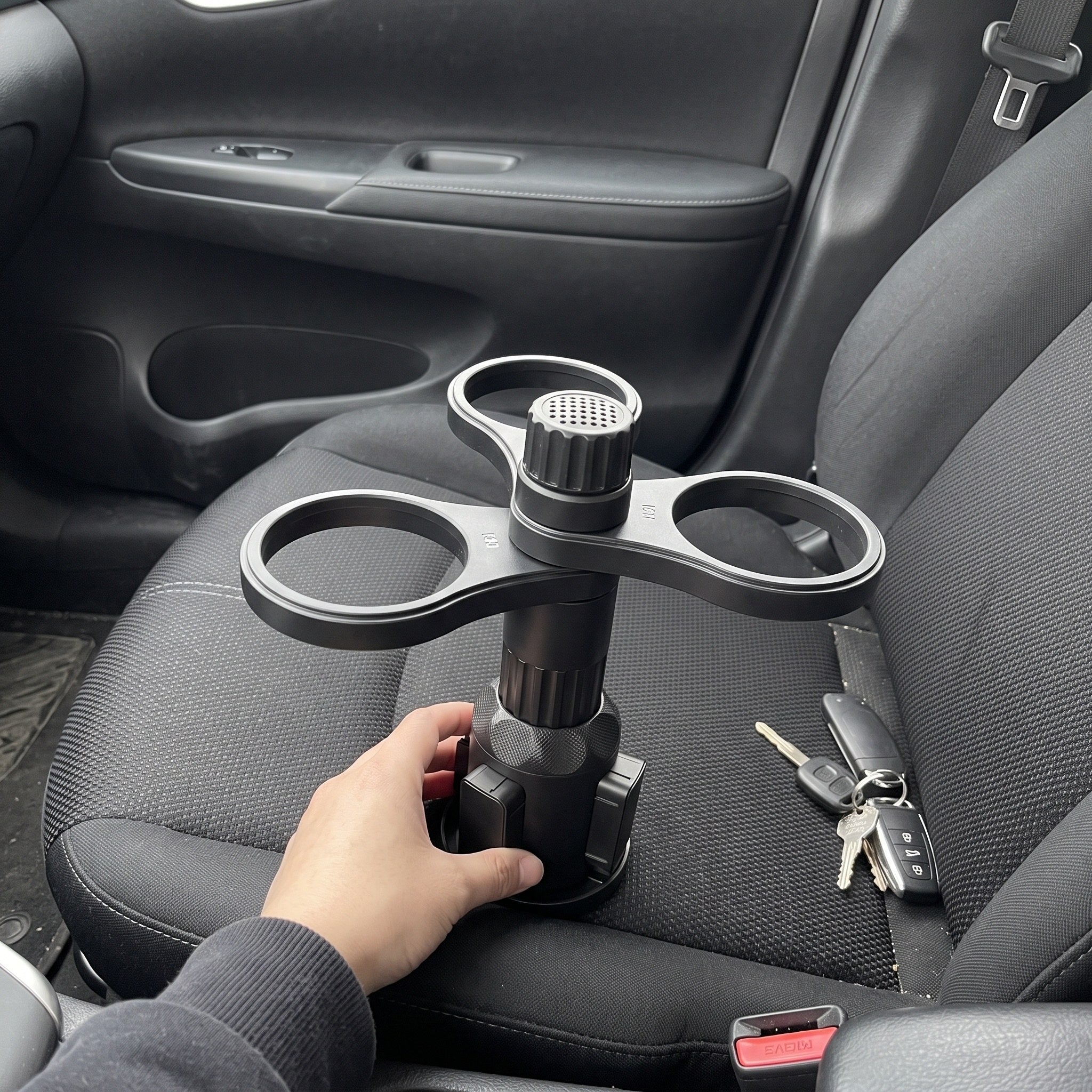 A hand holds the empty assembled holder on a car seat before installation