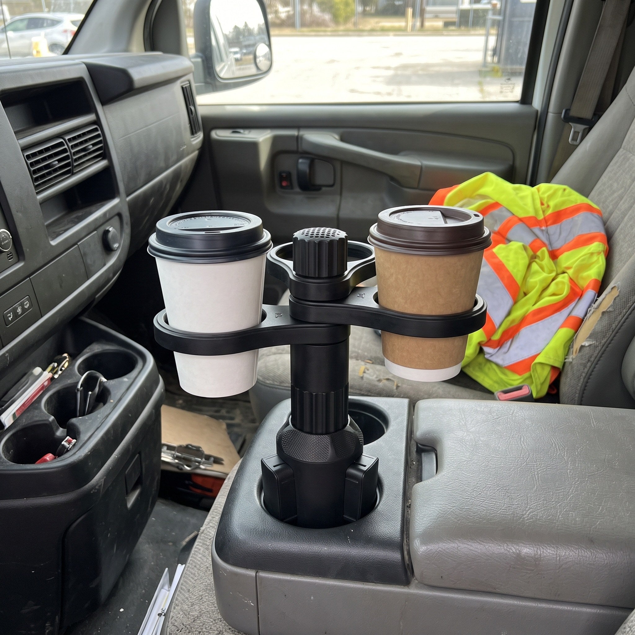 Two takeaway coffees in a parked work van beside a safety jacket
